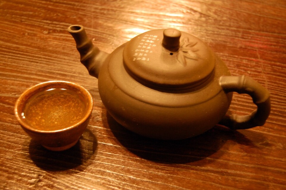 Illustrative stock photograph: Cup of green tea and tea pot on table. This may differ from the café's actual product.